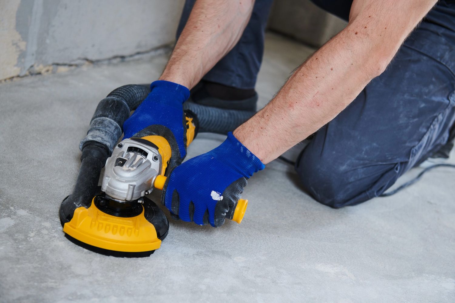 Worker polishing concrete floors in Houston with a handheld grinder for a smooth, professional finish.