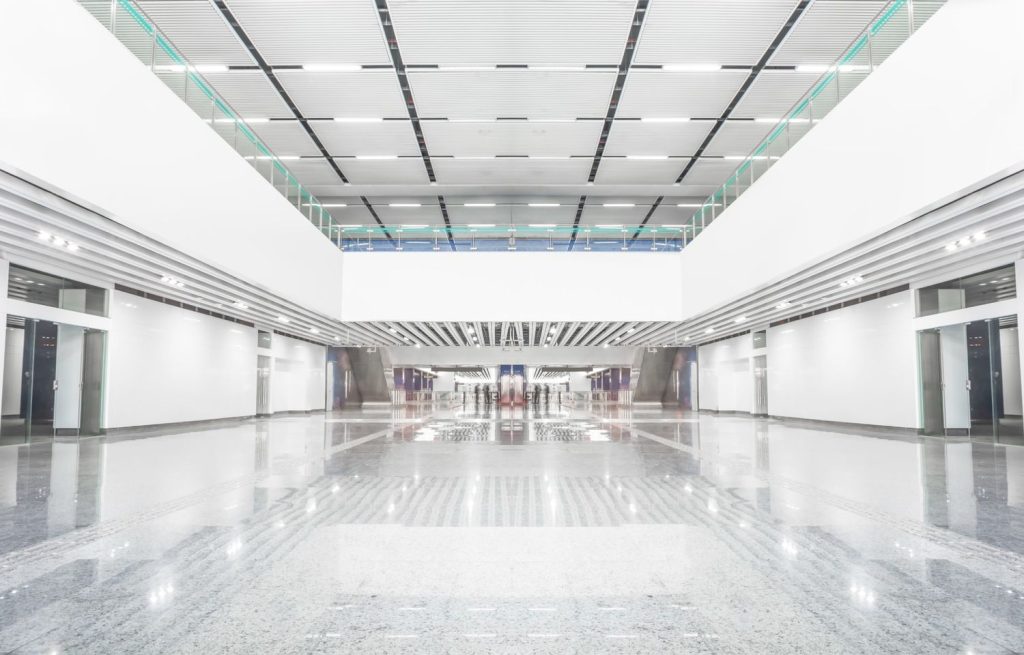Vast modern lobby with gleaming cement floors and white minimalist design, transformed by a professional cement polishing company in Houston to enhance aesthetics and functionality.