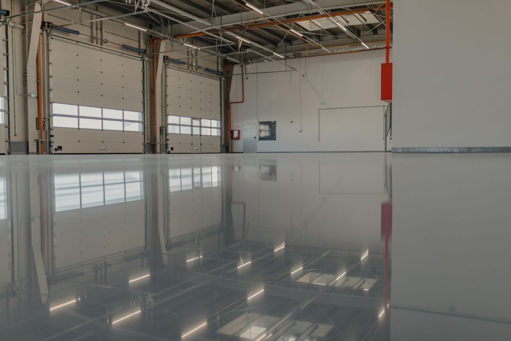 High-gloss gray epoxy refinished concrete flooring Houston with perfect mirror shine in a large commercial warehouse.