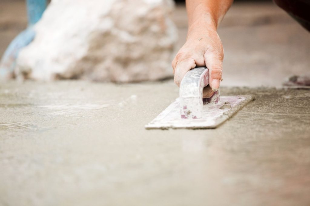 Installer using a trowel tool to smooth and level the wet finished cement flooring Houston during installation process.
