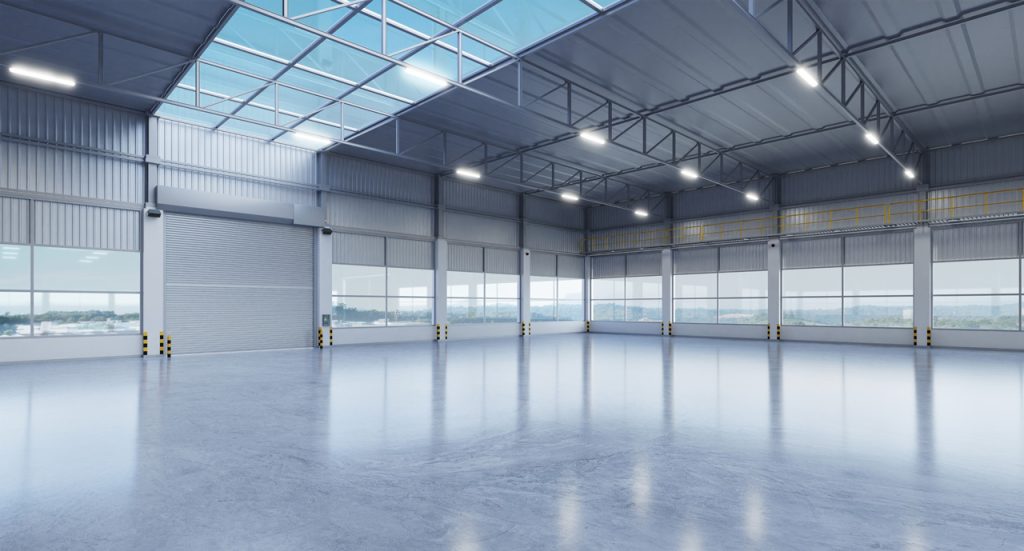 High-gloss shiny cement flooring Houston in a large industrial warehouse with steel trusses and bright natural skylights.