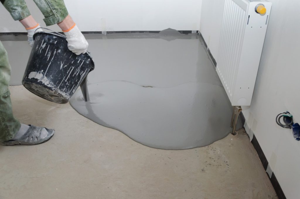 Professional contractor pouring self-leveling mixture for a high-quality finished cement flooring Houston project.