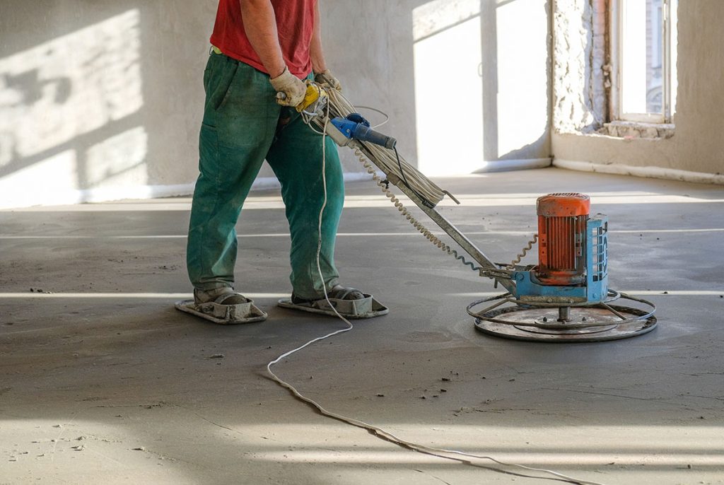 Skilled worker finishing a large room with durable and sleek refinished concrete flooring Houston industrial services.