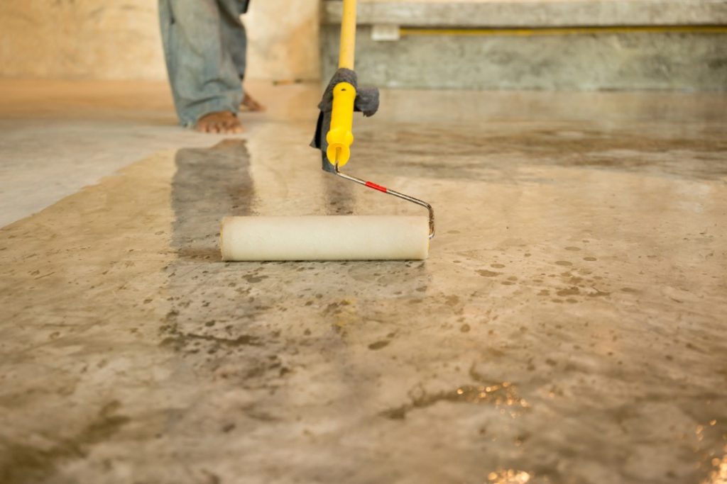 Residential concrete polishing floors Houston professional applying a clear protective sealant with a roller tool.