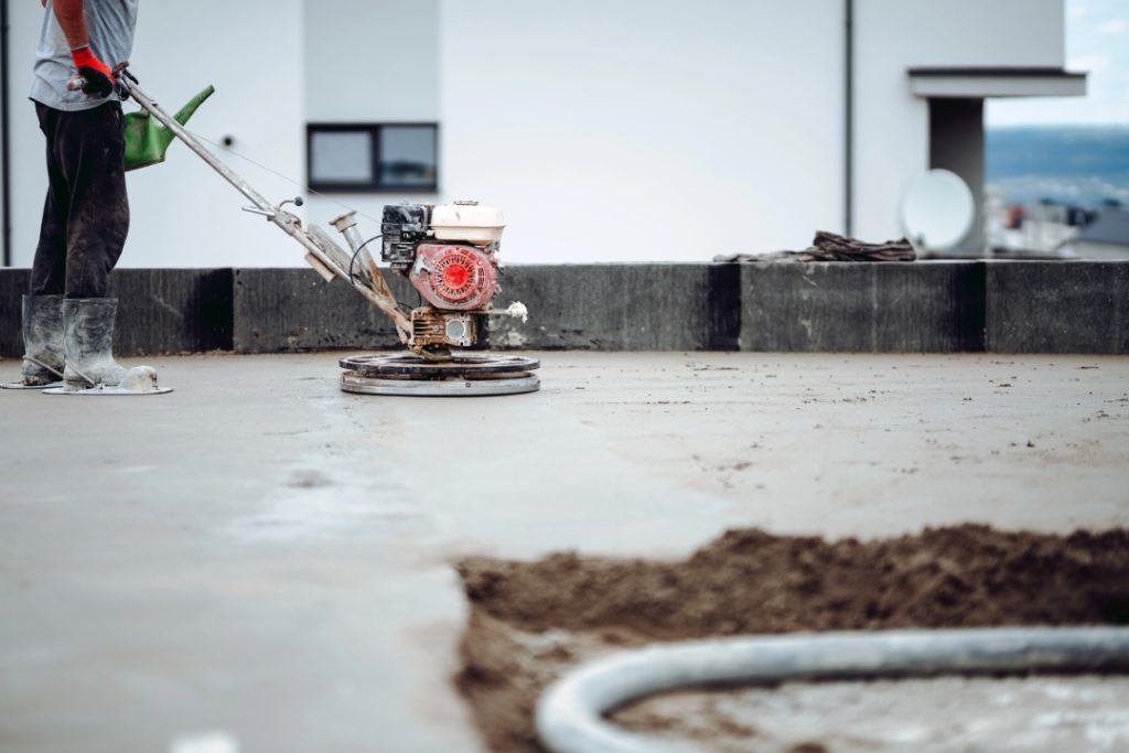 Worker operating a gas powered trowel for durable outdoor finished cement flooring Houston on a modern patio.