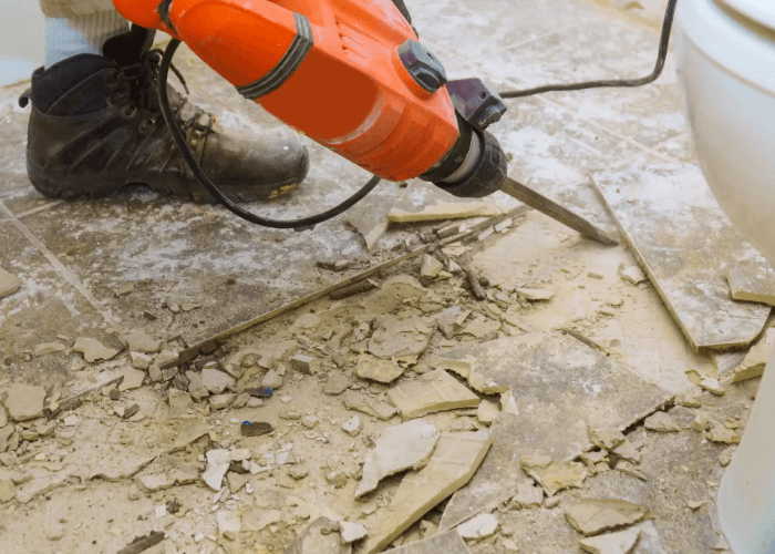 Professional floor removal service Houston technician uses a power chisel to strip old bathroom floor tiles.