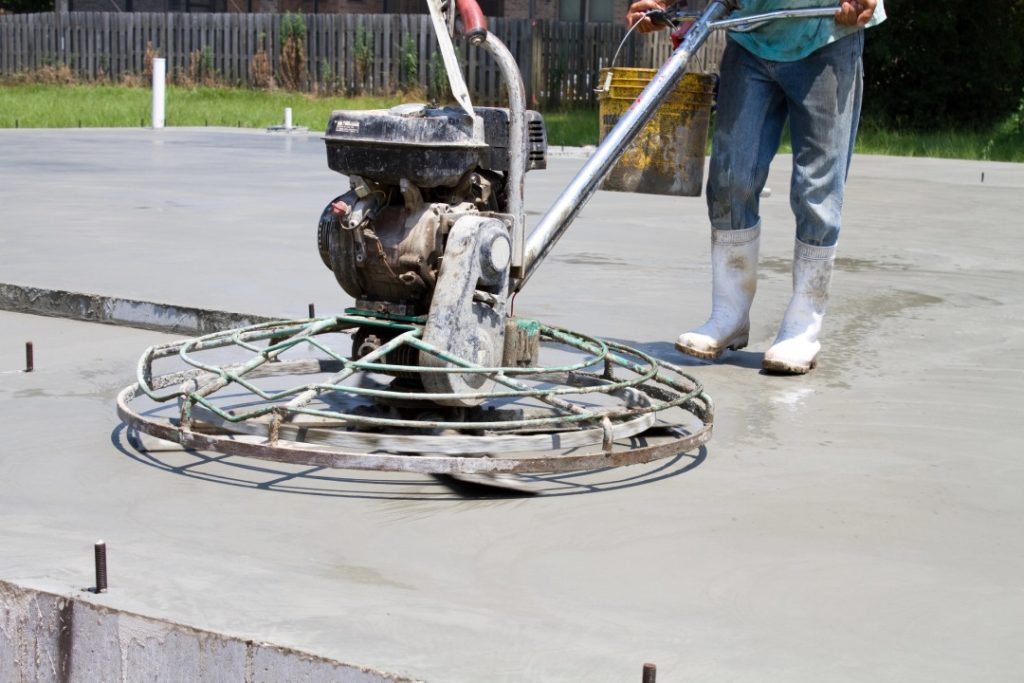 Industrial gas power trowel smoothing wet concrete for a high-quality shiny cement flooring Houston foundation.