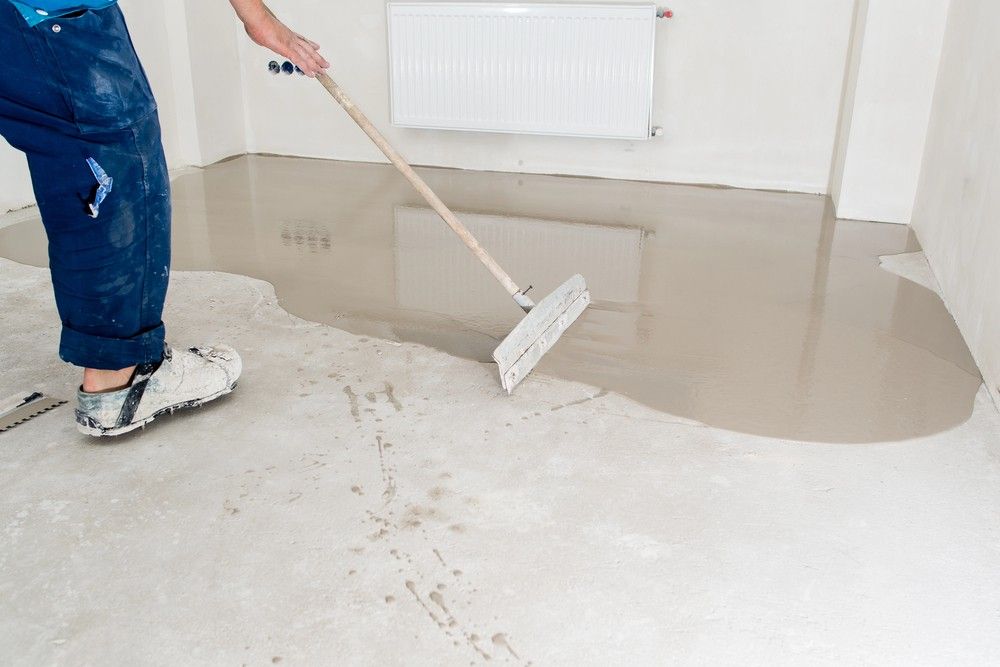 A worker wears spiked shoes while spreading leveling compound for heavy-duty polished cement floors Houston warehouses use. 