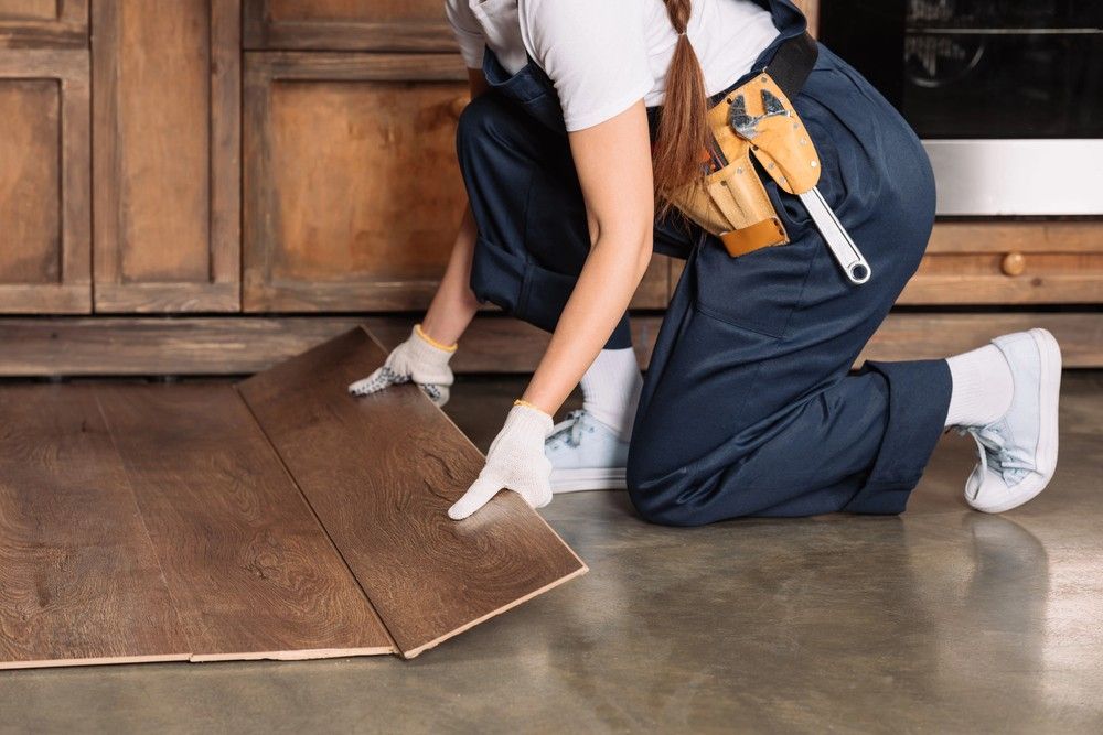 An installer lays dark wood laminate over a concrete base, an alternative look to industrial polished cement floors Houston. 