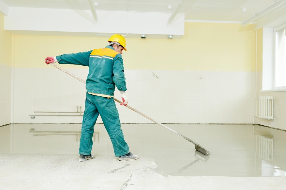 A construction worker applies a grey coating to create refinished concrete flooring Houston in a large room.
