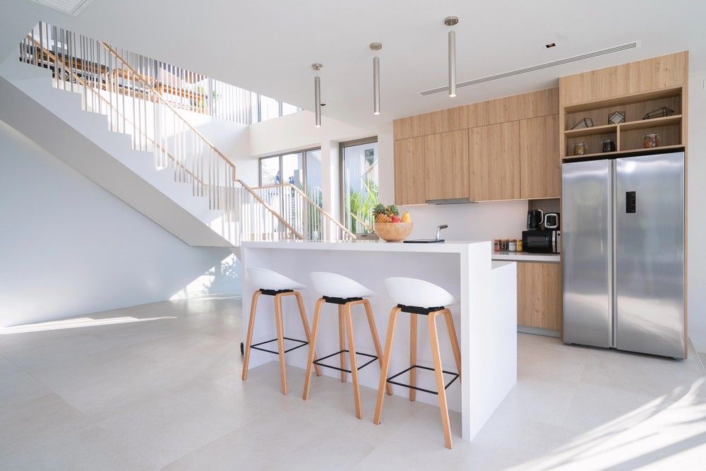 Minimalist kitchen by polished concrete contractors Houston with wood cabinets white island and open staircase.