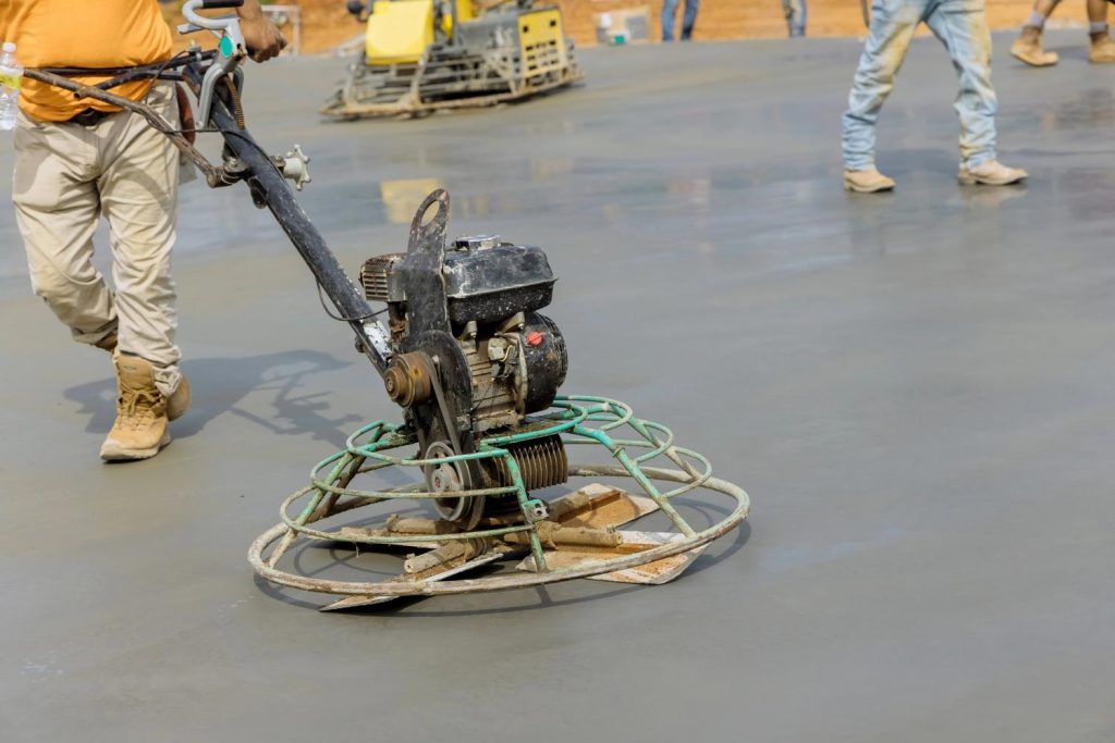 A worker uses a power trowel to smooth wet concrete for a high-quality shiny cement flooring Houston installation.