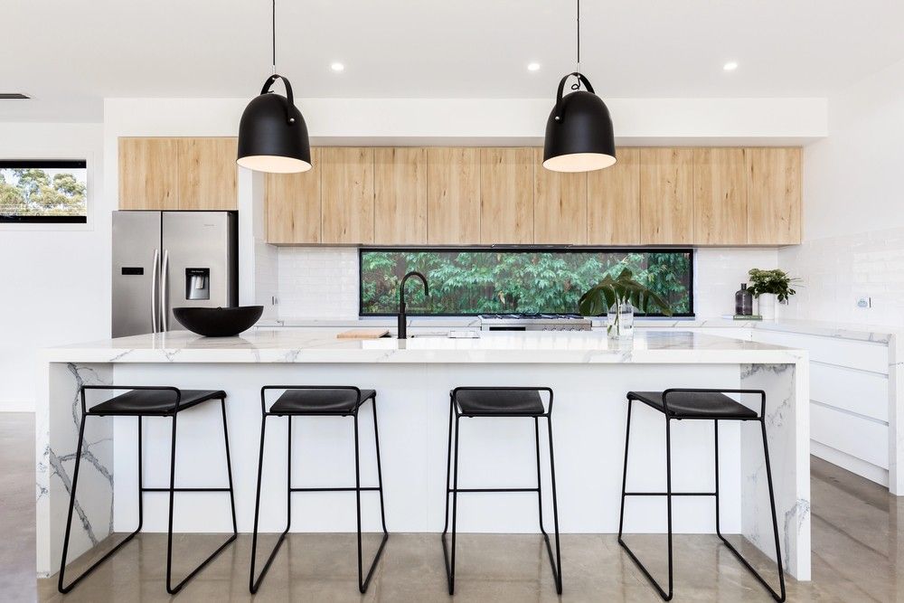 Sleek marble island designed by polished concrete contractors Houston with black barstools and pendant lights.