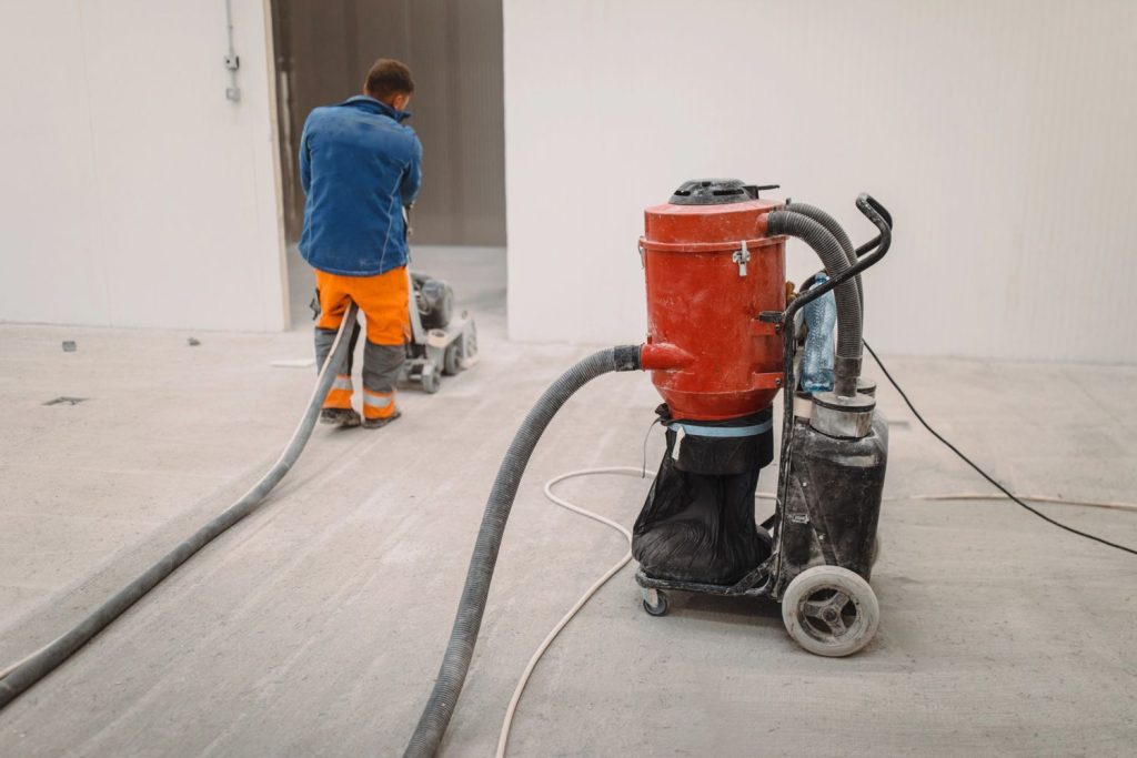 Worker polishing concrete floors in Houston with a grinding machine and vacuum for a clean, smooth finish.