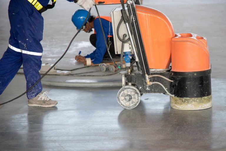 Workers using a floor grinder to create polished cement, showcasing skills of polished cement contractors Houston.