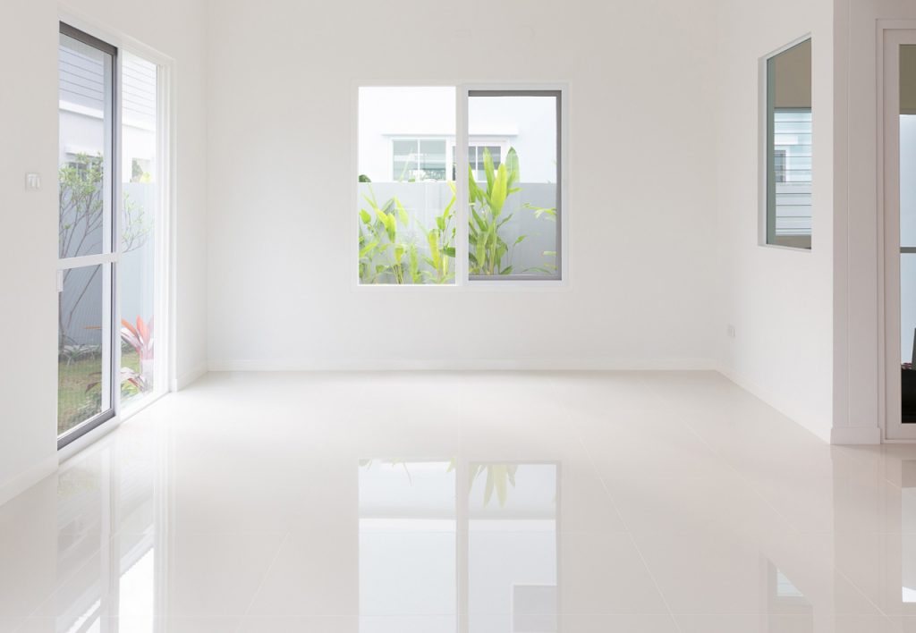 Elegant white shiny cement flooring Houston in a bright, minimalist modern home interior with large glass sliding doors.