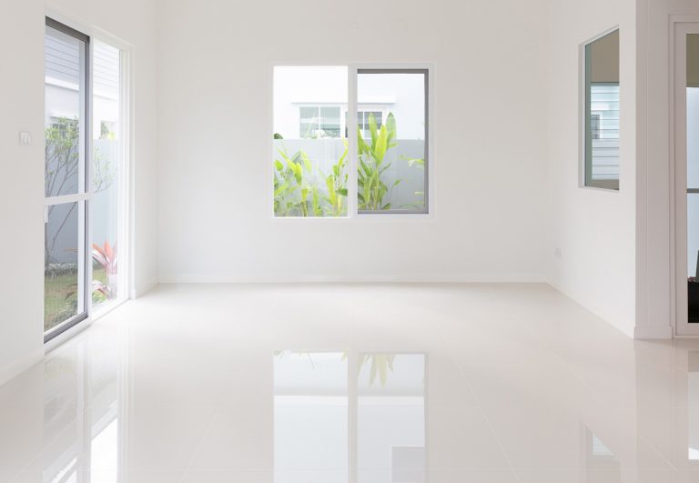 Elegant white shiny cement flooring Houston in a bright, minimalist modern home interior with large glass sliding doors.