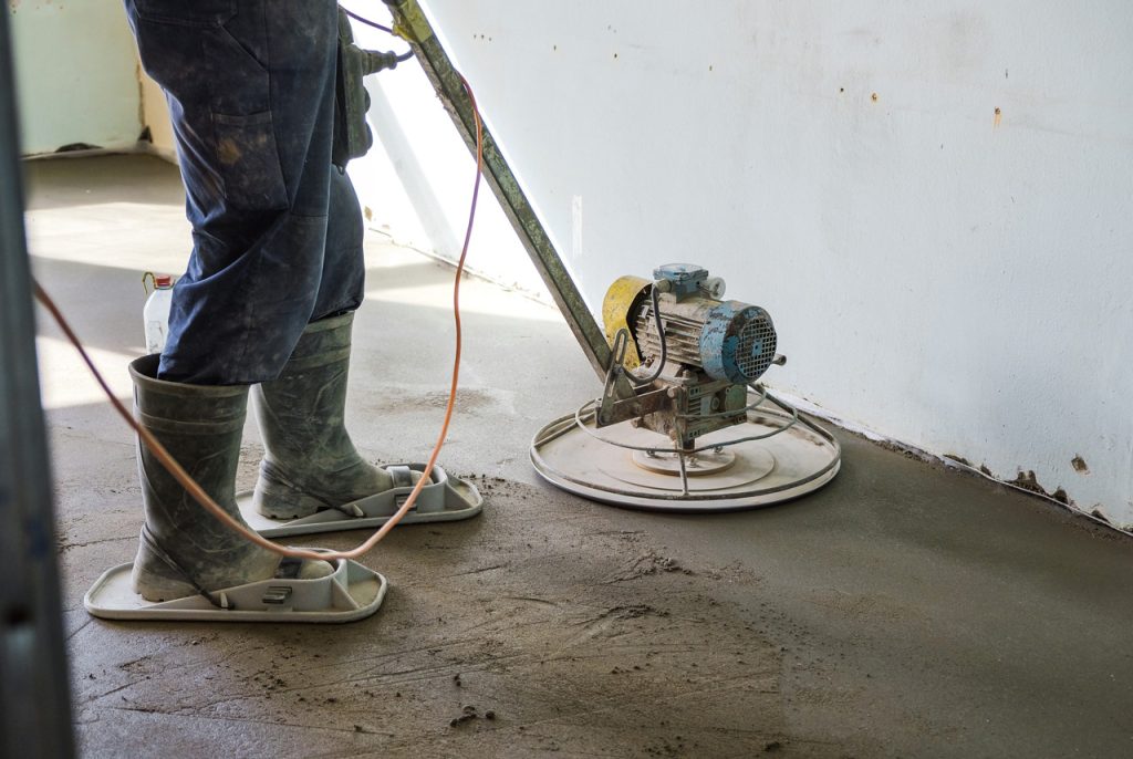 Skilled polished concrete contractors Houston finishing a fresh concrete floor using a specialized power trowel.
