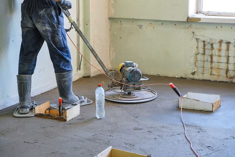 Professional worker using a power trowel for refinished concrete flooring Houston services in a large room.