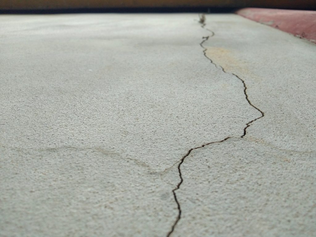 Close up of a long hairline crack needing repair on a grey finished concrete flooring Houston residential driveway.