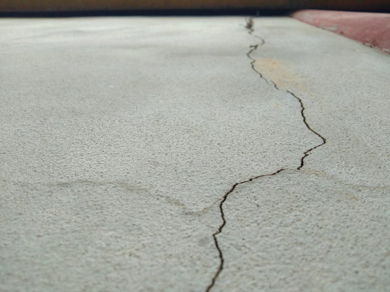 Close up of a long hairline crack needing repair on a grey finished concrete flooring Houston residential driveway.
