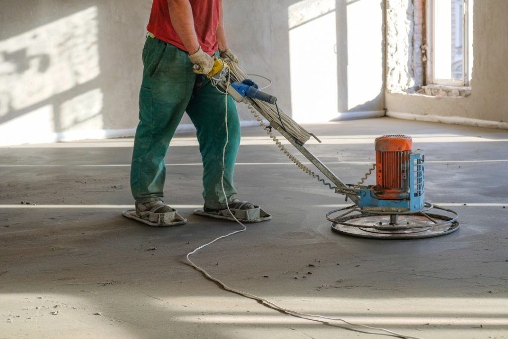 Professional contractor using a power trowel to achieve high quality finished cement flooring Houston indoors.