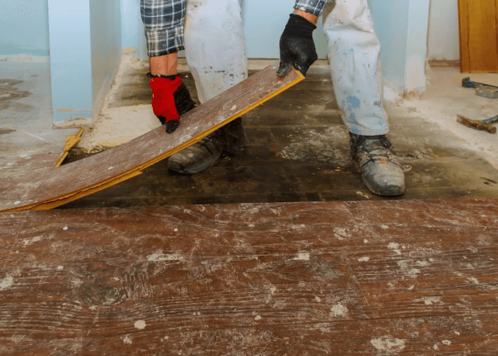 Professional floor removal service Houston technician manually lifting old laminate planks from a home subfloor.